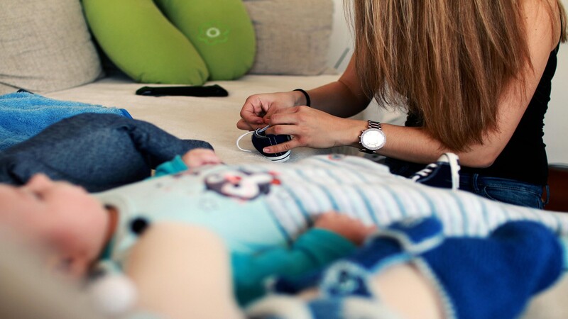 woman adjusting a baby's shoelace on a sofa