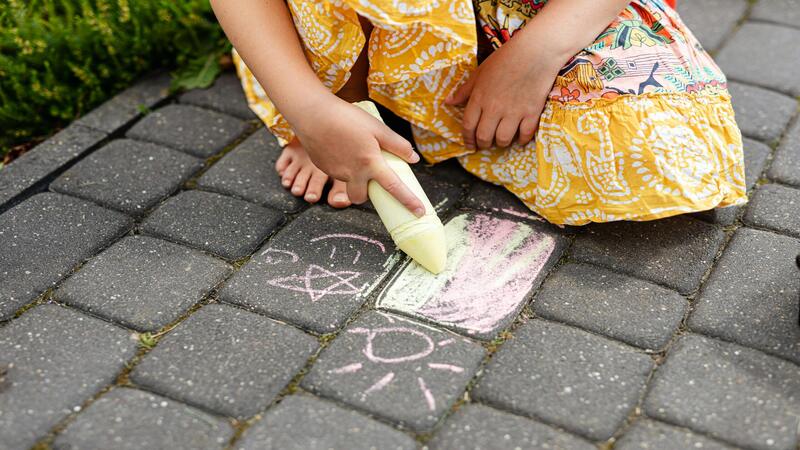 a girl drawing on the pavement using a large yellow chalk