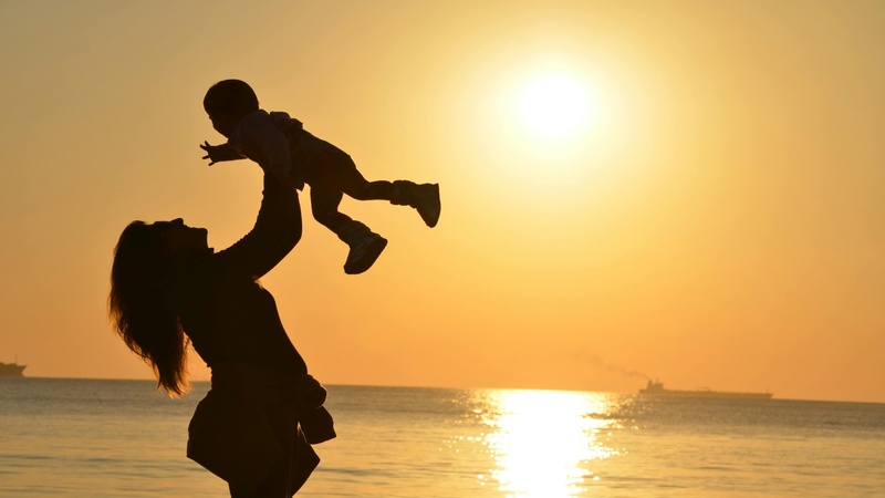 mother carrying her baby up high in a beach sunset background